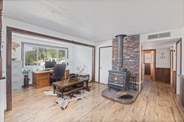 office space with visible vents, a wood stove, a textured ceiling, and light wood-style flooring
