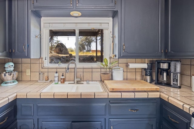 kitchen with tile countertops, a sink, blue cabinets, and decorative backsplash