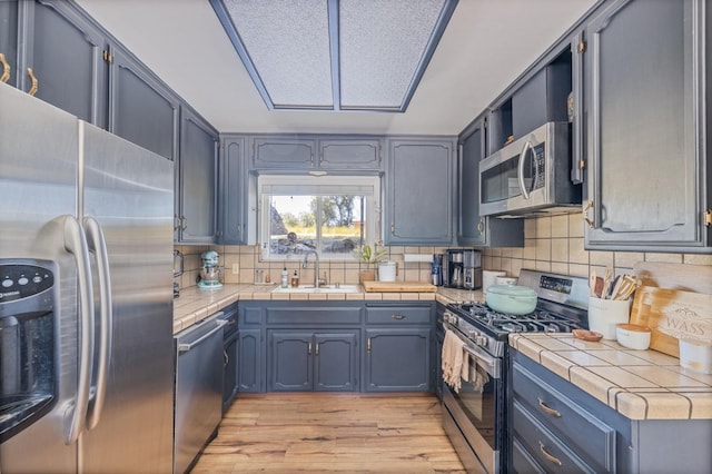kitchen with decorative backsplash, a sink, appliances with stainless steel finishes, tile counters, and light wood-type flooring