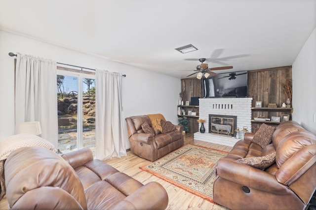 living area with a fireplace, wood finished floors, visible vents, and a ceiling fan
