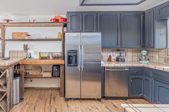 kitchen featuring stainless steel appliances, decorative backsplash, light wood-style flooring, tile countertops, and blue cabinets