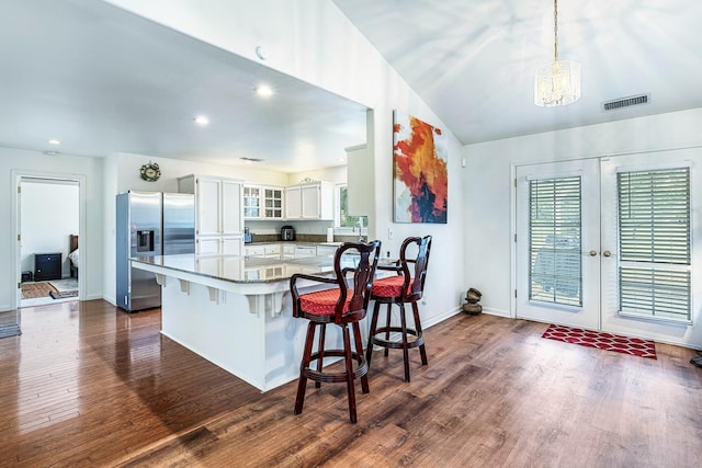 kitchen with a breakfast bar area, glass insert cabinets, visible vents, dark wood finished floors, and stainless steel refrigerator with ice dispenser