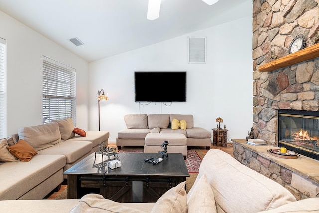 living room with visible vents, wood finished floors, a stone fireplace, and vaulted ceiling