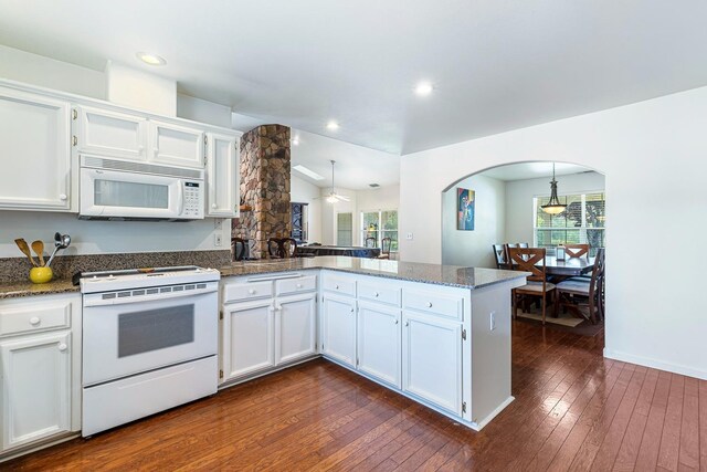 kitchen with arched walkways, a peninsula, a wealth of natural light, and white appliances