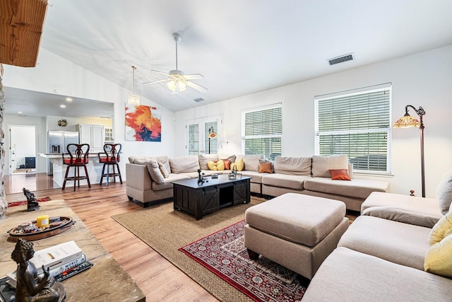 living room featuring light wood finished floors, a ceiling fan, visible vents, and vaulted ceiling