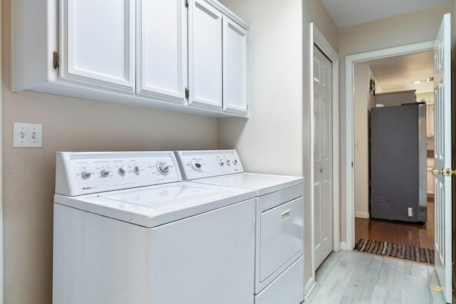 clothes washing area featuring light wood-style floors, cabinet space, and washing machine and dryer
