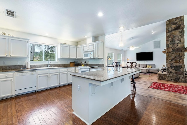 kitchen with a sink, a breakfast bar, dark wood-style flooring, white appliances, and a peninsula