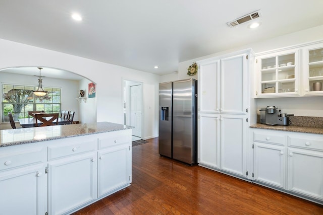 kitchen featuring visible vents, stainless steel refrigerator with ice dispenser, light stone counters, white cabinetry, and arched walkways