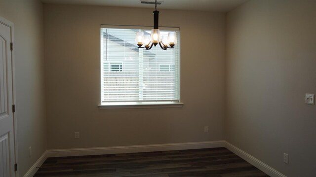 empty room featuring dark wood-type flooring, visible vents, a notable chandelier, and baseboards