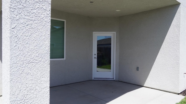 view of exterior entry with stucco siding and a patio area