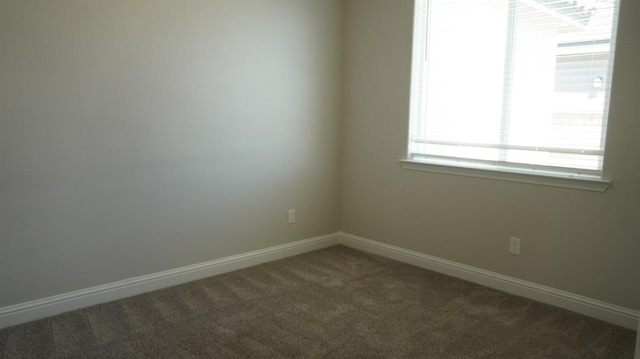 spare room featuring baseboards and dark carpet