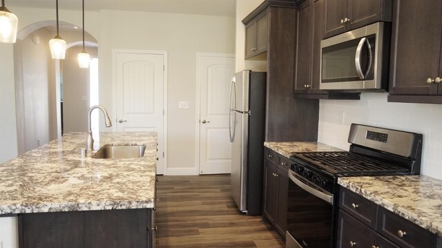 kitchen featuring a sink, stainless steel appliances, dark brown cabinetry, dark wood finished floors, and backsplash