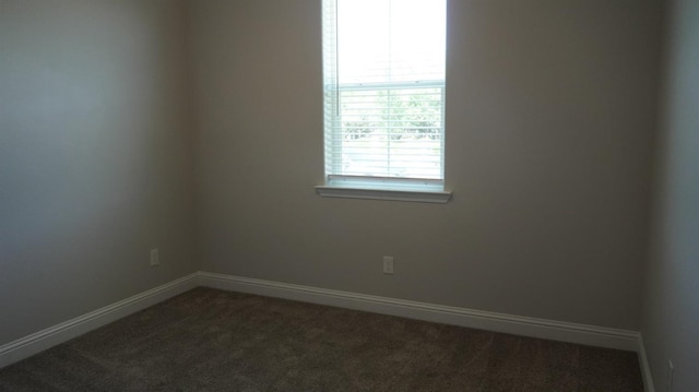 spare room featuring dark colored carpet and baseboards