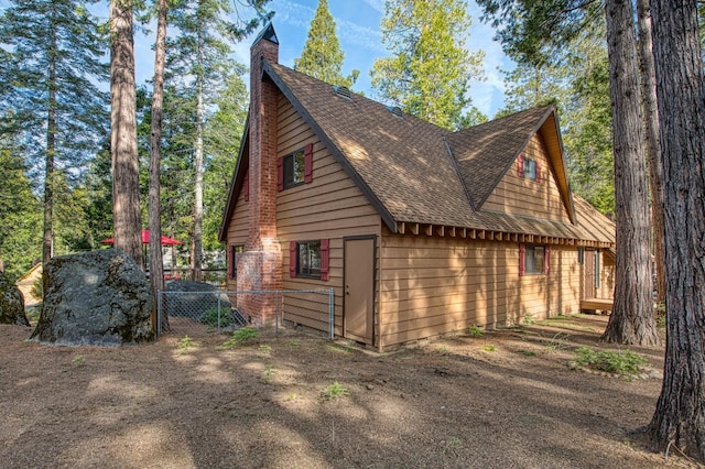 view of property exterior featuring fence, a chimney, and a shingled roof