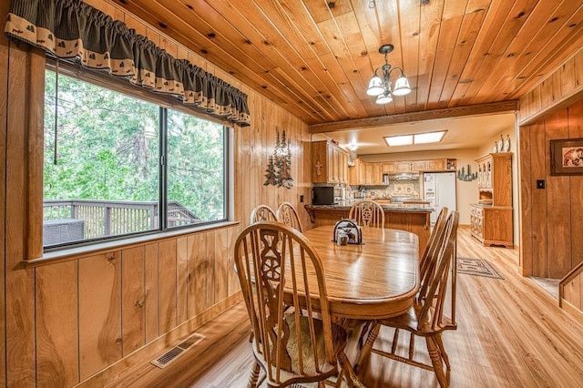 dining area featuring wooden walls, an inviting chandelier, visible vents, and light wood-style floors