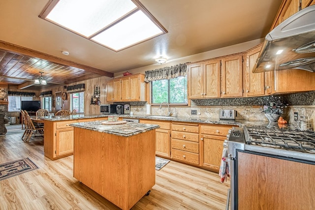 kitchen with light wood-style floors, a sink, a peninsula, and stainless steel range with gas cooktop