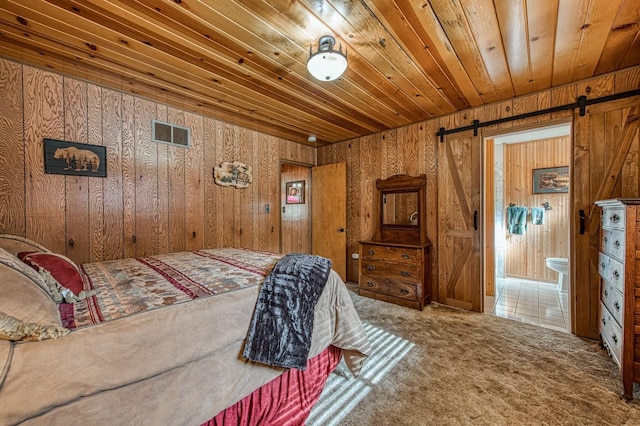 carpeted bedroom with connected bathroom, wood ceiling, a barn door, visible vents, and wooden walls