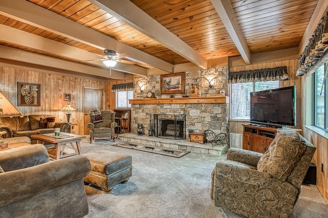 living area featuring beamed ceiling, ceiling fan, carpet floors, wooden walls, and a stone fireplace