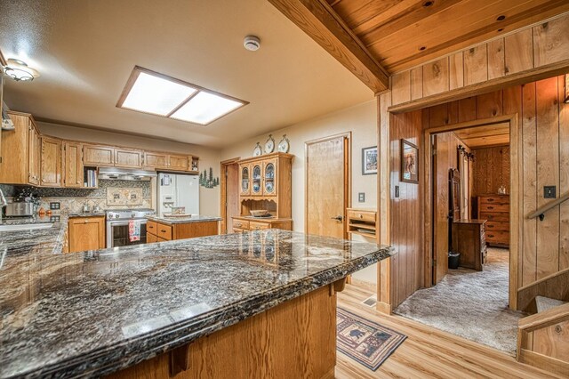 kitchen featuring tasteful backsplash, under cabinet range hood, wood walls, light wood-type flooring, and stainless steel range with gas stovetop