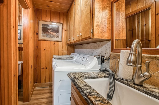 clothes washing area featuring a sink, washing machine and dryer, cabinet space, and wood walls