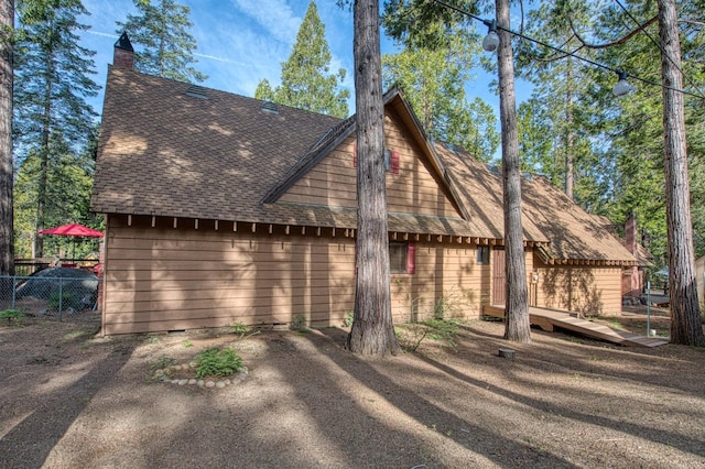 view of side of home with a deck, fence, and a shingled roof