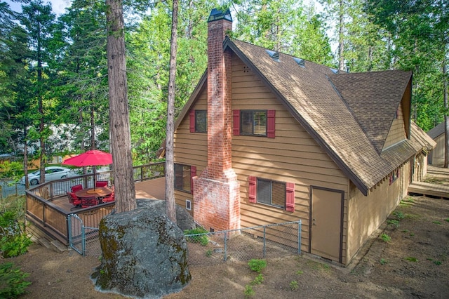 back of property featuring a deck, a shingled roof, fence, and a chimney