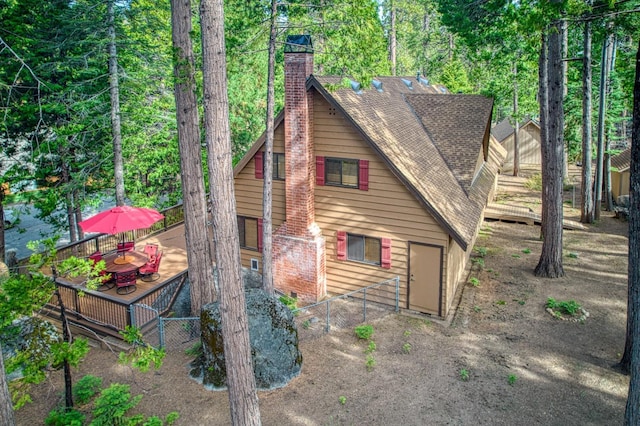 view of property exterior featuring a chimney, fence, a wooden deck, roof with shingles, and outdoor dining space