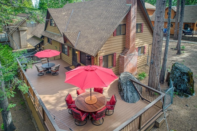 back of house with a deck, outdoor dining area, a chimney, and roof with shingles