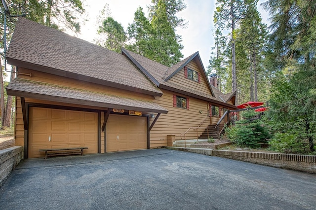 view of side of home featuring a garage, stairway, aphalt driveway, and roof with shingles
