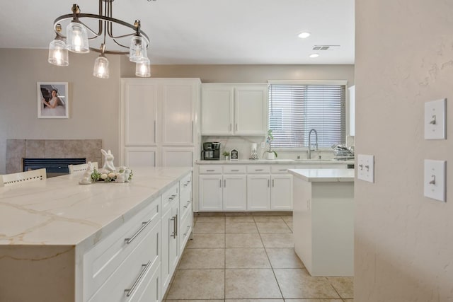 kitchen featuring light stone counters, light tile patterned floors, white cabinets, a sink, and a kitchen island