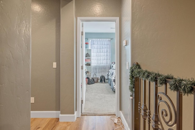 corridor featuring baseboards, a textured wall, and light wood-style floors