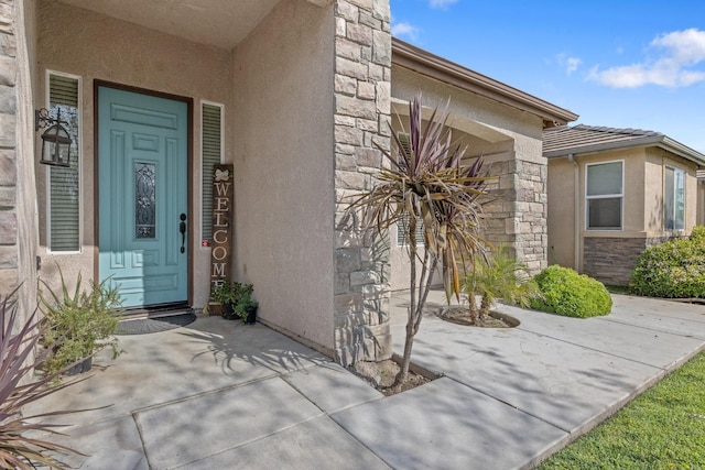 property entrance featuring stucco siding, a patio area, and stone siding