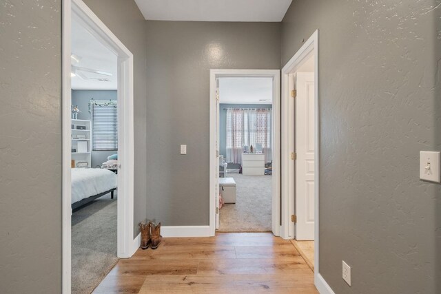 hallway with baseboards, wood finished floors, and a textured wall