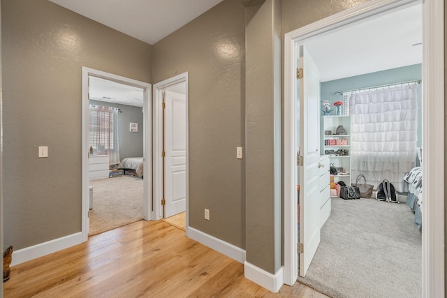 hall featuring baseboards, light wood-type flooring, and a textured wall
