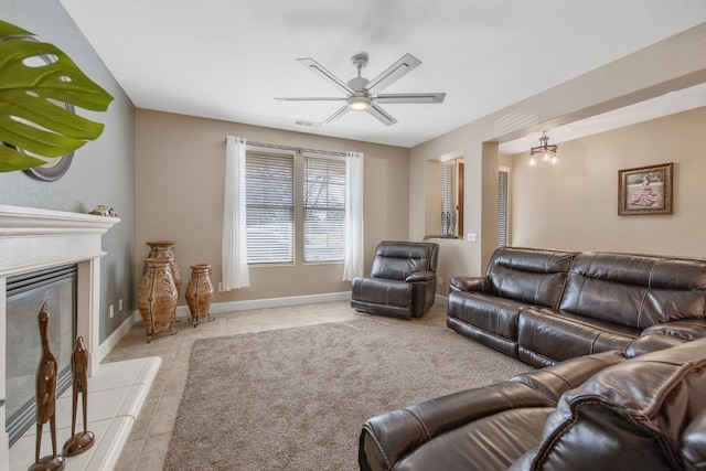 living area featuring a tile fireplace, light tile patterned flooring, a ceiling fan, and baseboards