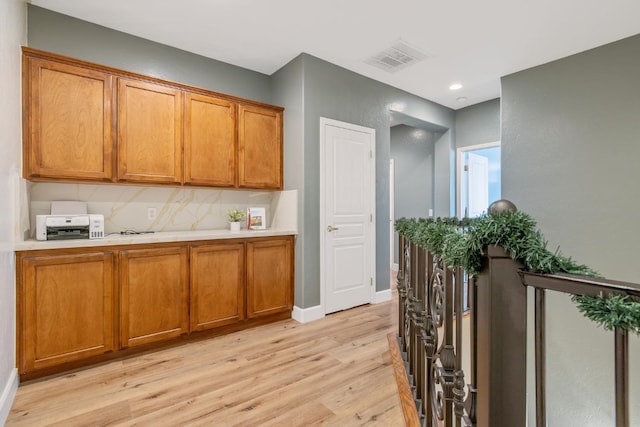 kitchen with brown cabinetry, light wood-style floors, light countertops, baseboards, and visible vents