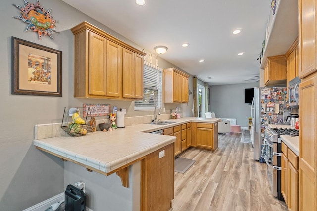 kitchen with a sink, light wood-style floors, stainless steel appliances, recessed lighting, and a peninsula
