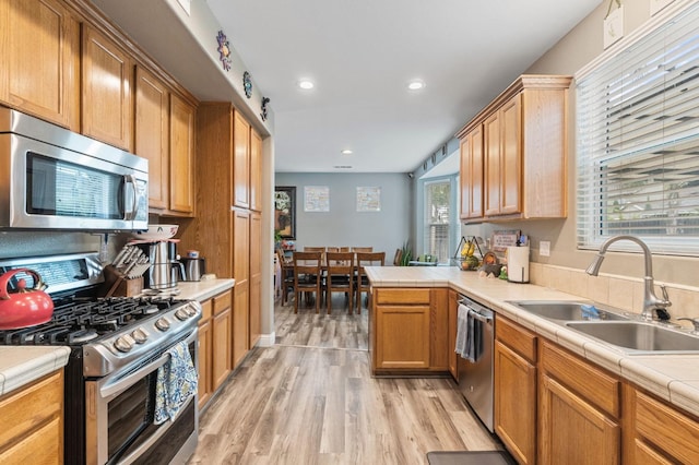 kitchen featuring light wood finished floors, a sink, stainless steel appliances, a peninsula, and tile countertops