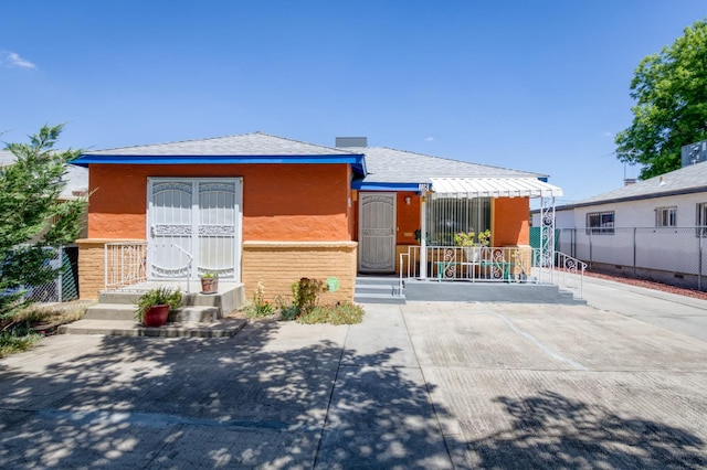 view of front of house with stucco siding, fence, a shingled roof, and a porch