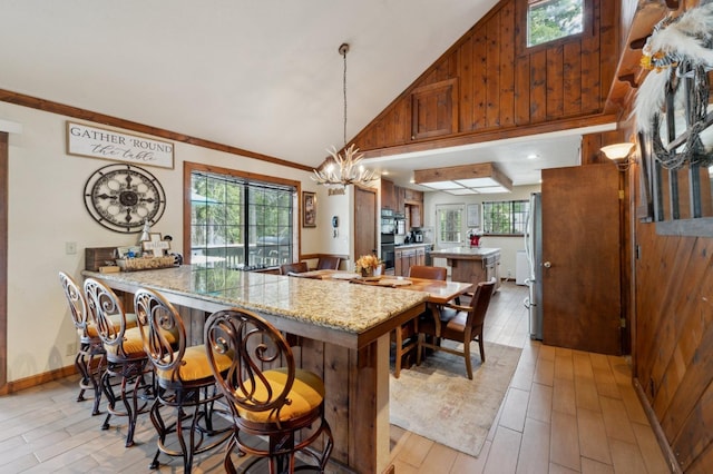 kitchen with light wood-style flooring, a chandelier, brown cabinets, high vaulted ceiling, and a peninsula