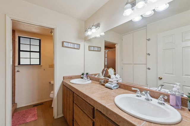full bathroom with toilet, a sink, wood finished floors, and visible vents