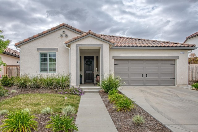mediterranean / spanish home featuring driveway, a tiled roof, stucco siding, an attached garage, and fence