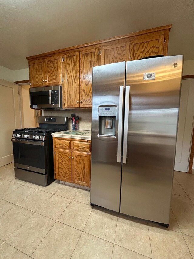 523 W Yosemite, Madera, CA 93637 - kitchen featuring brown cabinetry, tile countertops, appliances with stainless steel finishes, and light tile patterned floors