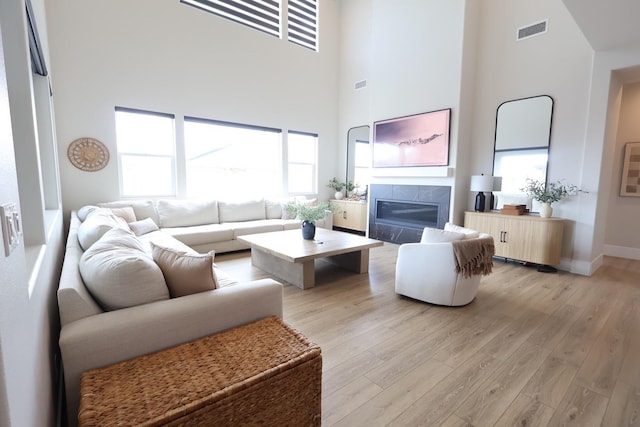 living room featuring a tile fireplace, a high ceiling, light wood-type flooring, visible vents, and baseboards
