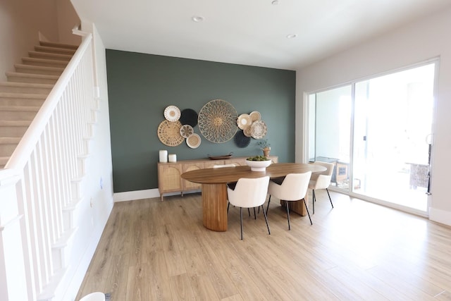 dining area with baseboards, an accent wall, light wood-type flooring, and stairway