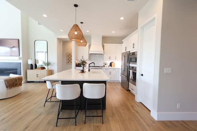 kitchen with light wood finished floors, stainless steel appliances, a kitchen bar, custom range hood, and light countertops