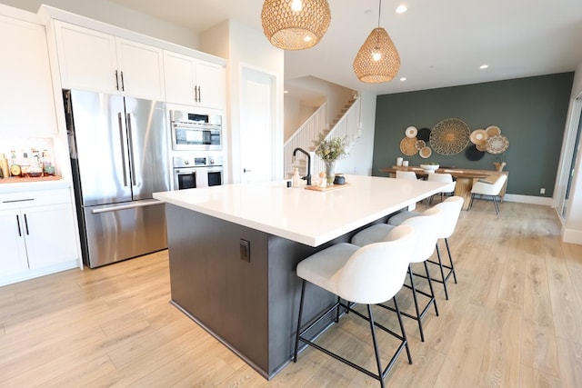 kitchen featuring appliances with stainless steel finishes, white cabinetry, a kitchen island with sink, and light wood-style flooring