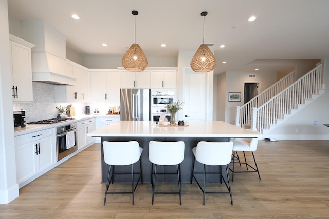 kitchen with a center island, custom exhaust hood, appliances with stainless steel finishes, and light wood-style flooring