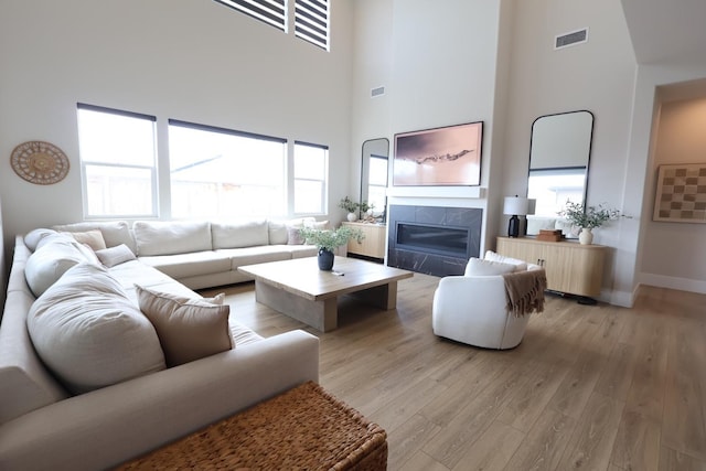 living room featuring a healthy amount of sunlight, visible vents, light wood-type flooring, and a high ceiling
