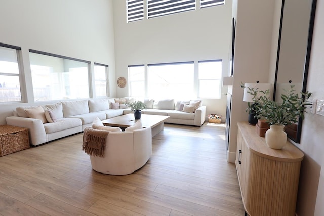 living area featuring a towering ceiling, light wood-style floors, and plenty of natural light